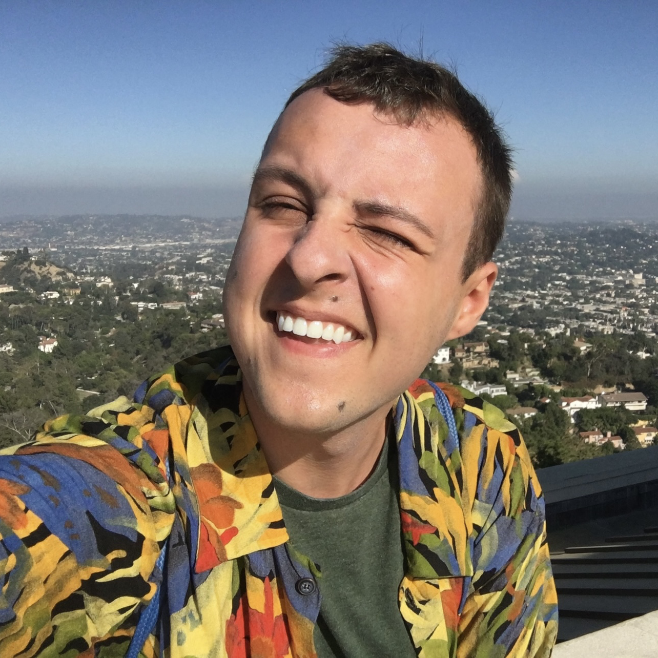 Eric smiling at the camera under a blue sky with Runyon Canyon Park behind him.